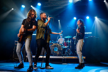 Rock band performing energetically on stage under blue lights