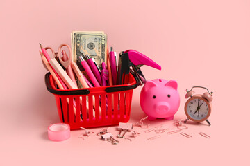 Shopping basket with different school stationery, money and piggy bank on pink background