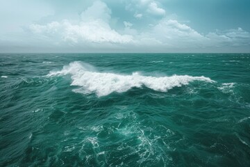 Fototapeta premium Waves crashing against the turquoise ocean under a cloudy sky during the day