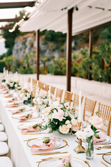 Festive table with bouquets of flowers and small pomegranates on plates stands under a canopy in the garden