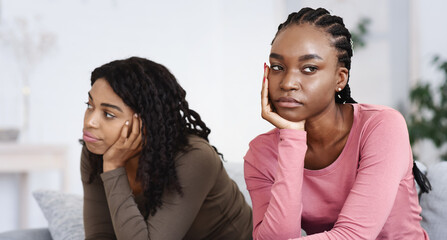 Two upset african american women sitting apart on sofa at home, had quarrel, copy space. Frustrated...