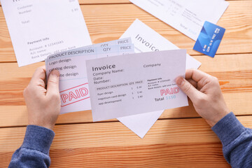Obraz premium Paying bills. Man with credit card and invoices at wooden table, top view