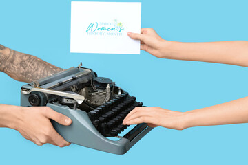 Hands holding vintage typewriter and festive postcard with text MARCH IS WOMEN'S HISTORY MONTH on blue background