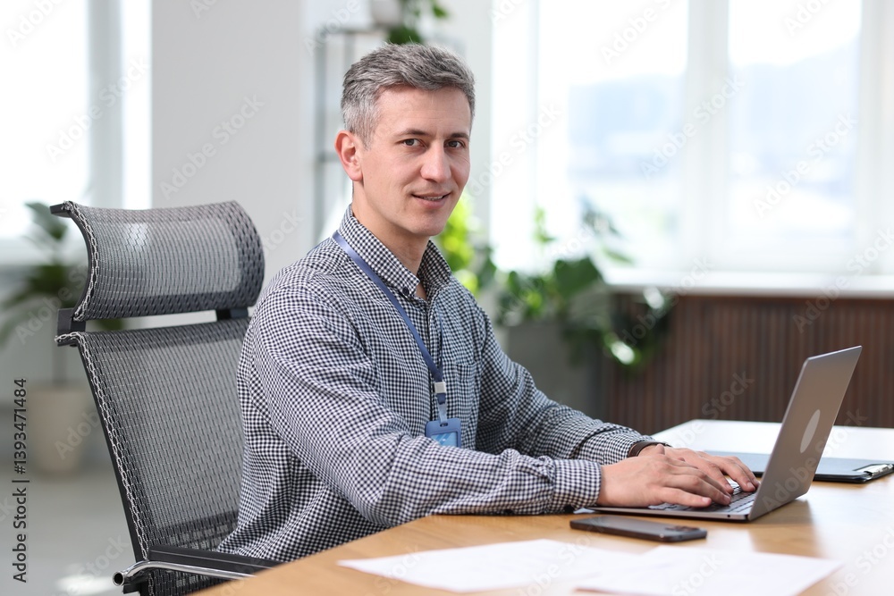 Poster smiling engineer working with laptop at table in office