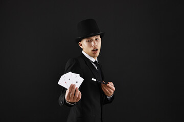Illusionist pointing magic wand on playing cards against black background