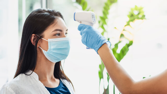 Measures to prevent people with fever. Manager checking body temperature of client at beauty salon, side view - Powered by Adobe