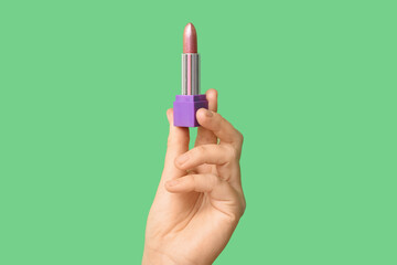 Hand holding lipstick on green background