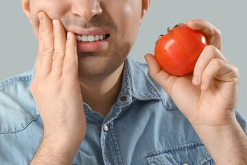 Young man with tomato suffering from toothache on light background, closeup