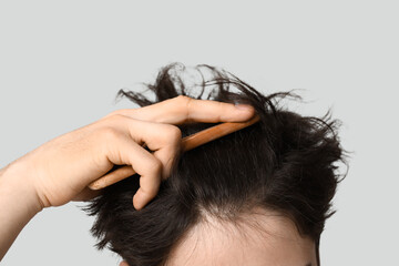 Naklejka premium Young man combing hair on grey background, closeup