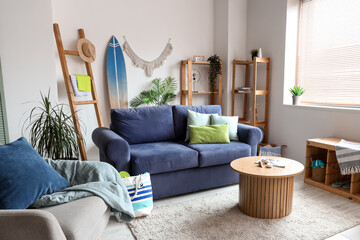 Interior of light living room with blue sofa, surfboard and coffee table