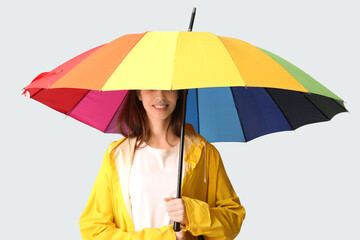 Young happy woman in raincoat with opened colorful umbrella on grey background
