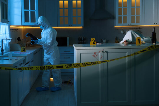 Forensic expert with camera working at crime scene and dead woman's body in dark room