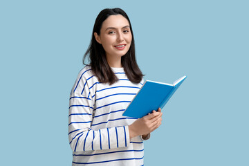 Fototapeta premium Young pretty woman reading book on blue background
