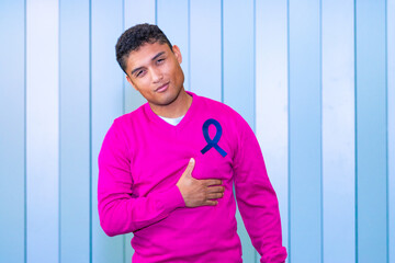 Latino man in pink sweater with cancer awareness ribbon, hand on chest