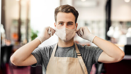 Personal and client safety. Young man barber putting on protective mask at barbershop, close up