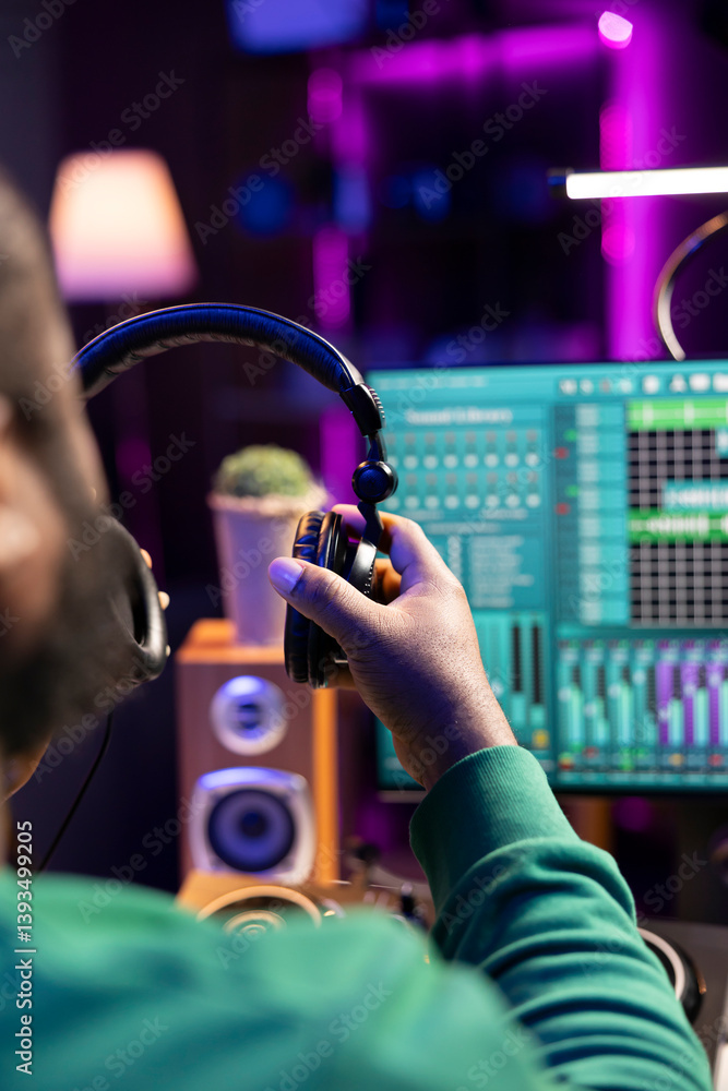 Poster Music producer using his headphones for a mix and master session, adding sound effects and adjusting volume levels on mixing console and amplifier. Digital audio software to edit tracks. Close up.