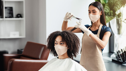 Hairdressing services during the coronavirus. Hairdresser cutting hair of african woman, both...