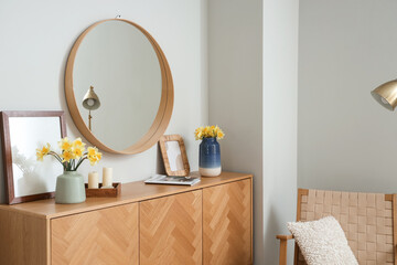 Chest of drawers, armchair and vase with narcissus flowers in living room