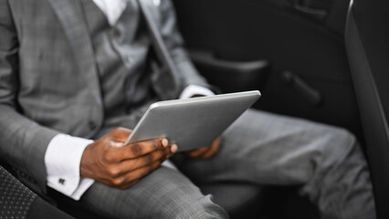 Cropped of african american businessman going by company car to business meeting, holding digital tablet, copy space. Unrecognizable black entrepreneur siting on back car seat with pad, top view