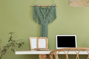 Laptop with frames on desk and houseplant near green wall in office