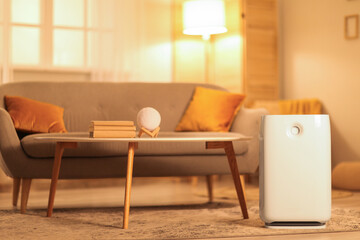 Stylish sofa and humidifier near coffee table in living room at evening