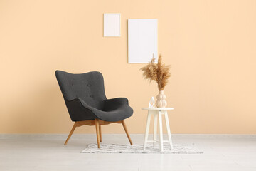 Cozy black armchair, pampas grass and frames on beige wall in room
