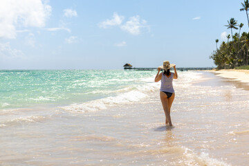 Woman walking along a tranquil beach enjoying warm weather and gentle waves in a tropical paradise