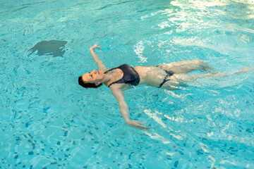 Woman enjoying relaxation while floating in a clear swimming pool in a sunny location during...