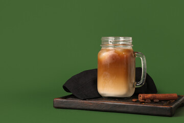 Mason jar of iced latte with cinnamon and coffee beans on green background