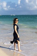 Woman walks barefoot along sandy beach, enjoying the tropical ocean breeze in a vibrant seaside setting