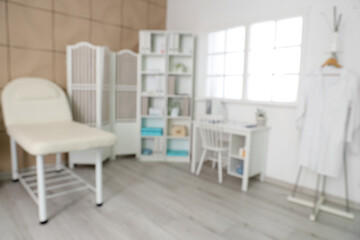 Blurred view of medical office with couch, folding screen and doctor's workplace