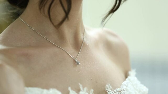 A close-up shot of a bride's delicate hand touching her neck, adorned with a silver necklace. Perfect for wedding, beauty, or fashion-related projects.