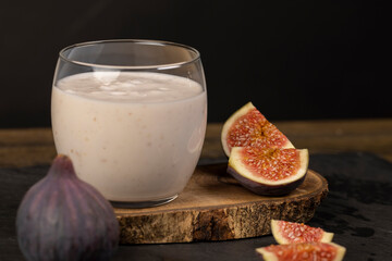 sliced fig fruit and a glass of low fat yogurt on a wooden table, sweet fig fruits and a glass of...