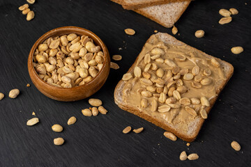peanut butter on a piece of bread and roasted peanuts on the table, view from above