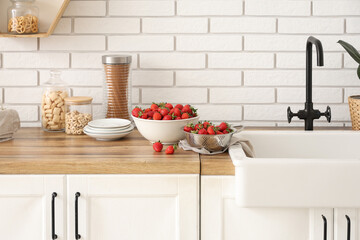 Bowl and colander with tasty strawberries on counter in kitchen