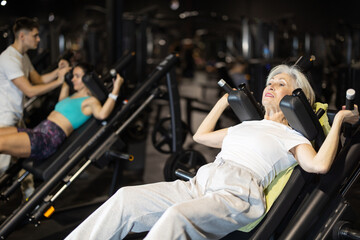 In gym, senior woman uses hack squat machine to strengthen muscles. Series of repetitions to...