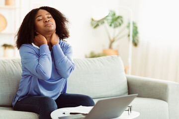Exhausted Person. Portrait of tired african american lady sitting on couch massaging sore neck, feeling pain after hard work, copy space. Black woman suffering from inflammation, student taking break