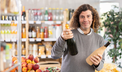 Adult man buyer chooses bottle of wine or champagne in grocery store