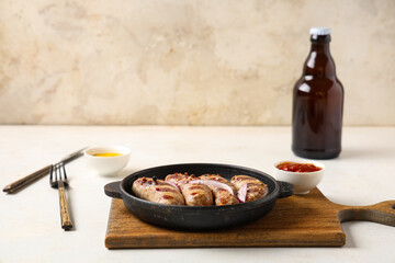 Frying pan with tasty grilled sausages, bowls of sauces and bottle of beer on white background