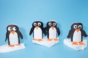 Handmade penguin figurines made from recycled toilet paper rolls on Styrofoam icebergs. Kids' winter craft project with arctic animal theme. Design for poster, banner, greeting card, and invitation.