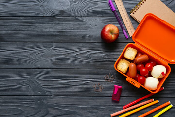 Lunch box with tasty food and school stationery on dark wooden background