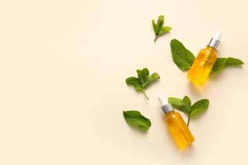 Bottles of essential mint oil and green leaves on beige background