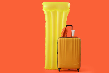 Inflatable mattress and suitcase on orange background. Travel concept
