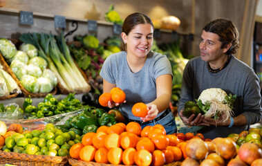 Caucasian man and woman looking to buy mandarin oranges and vegetables in local market