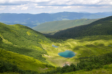 Breathtaking view of a serene mountain landscape featuring lush green valley and crystal clear lake Vorozheska nestled between rolling hills. Carpathian Mountains, Ukraine
