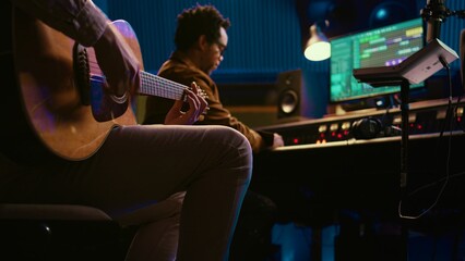 Creative musician singing guitar in professional studio control room, recording his tracks with...