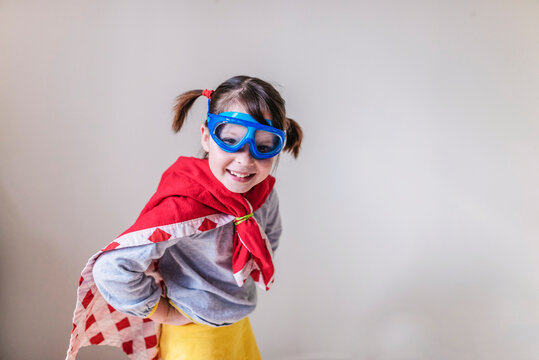 Portrait of a smiling girl dressed as a female superhero in a cape and swimming goggles