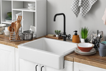Ceramic sink, clean dishes, and shelving unit on wooden kitchen counter