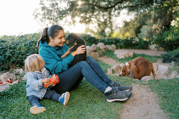 Fototapeta premium Little girl sits near her mother raising a small puppy in her arms