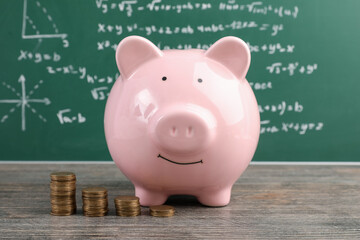 Piggy bank with coins on table near green blackboard. Student loan concept